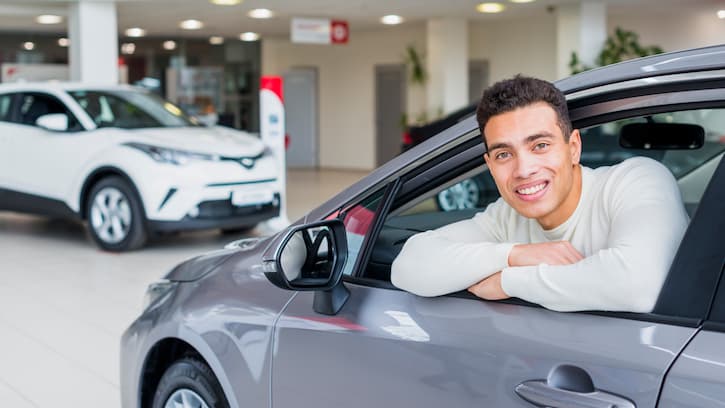 Homem sorridente na janela do motorista do seu novo carro pequeno, comprado com o consórcio de veículos.
