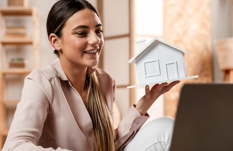 Mulher segurando uma casa em miniatura de papel, simbolizando o ganho de capital na venda de imóvel.