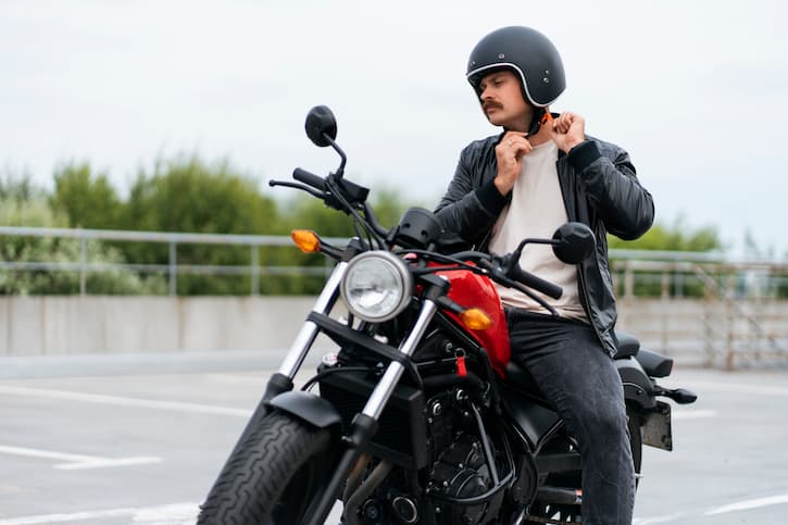 Homem ajustando o capacete preto enquanto está sentado na sua moto, adquirida através do consórcio de moto.