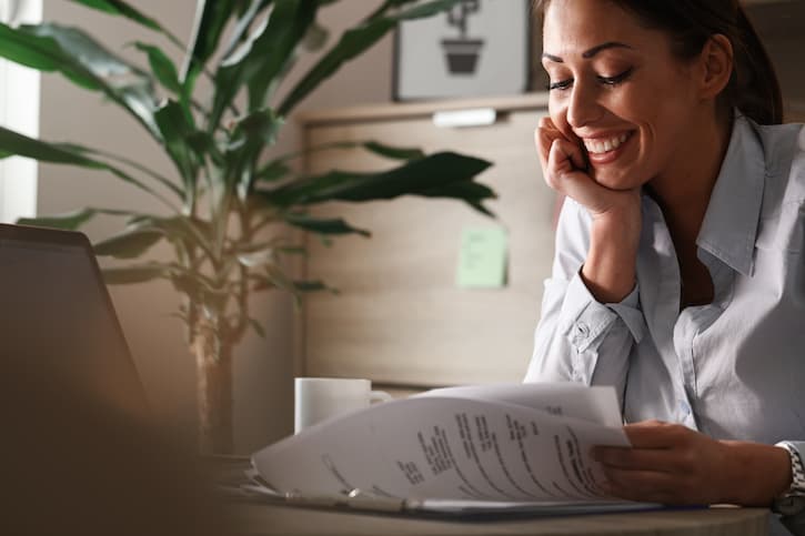 Mulher na mesa do seu escritório, sorrindo enquanto avalia as possibilidades no contrato da sua carta de crédito contemplada.