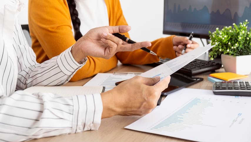 Foco na mesa, papéis de controle financeiro e mãos que analisam linhas de crédito.