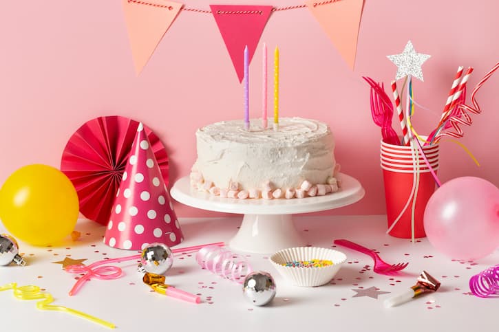 Mesa com bolo de aniversário e outros acessórios como copos, balões e confetes de uma festa de 15 anos.